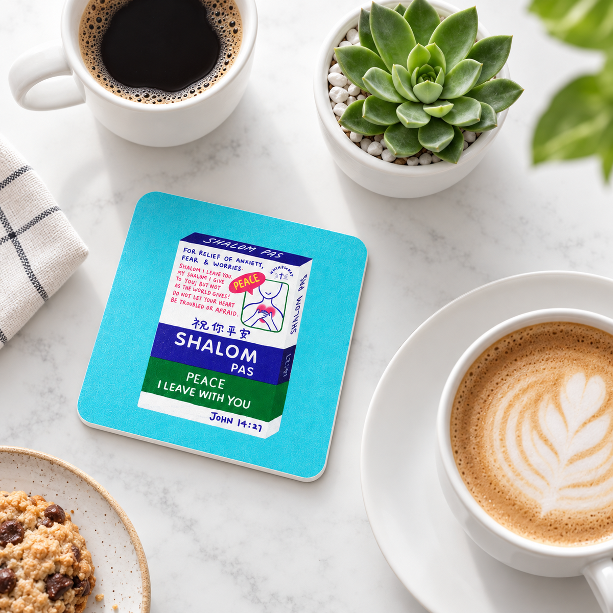 Shalom Pas Love Supermarket Christian coaster with white sides styled on a bright tabletop with coffee and greenery