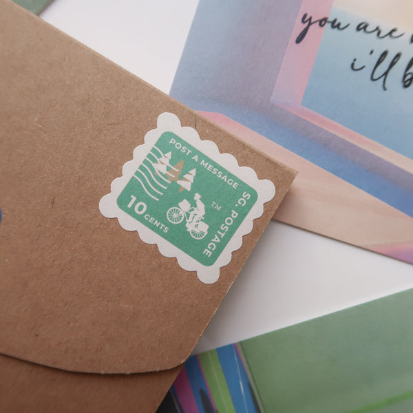 A close-up of an envelope adorned with a 10-cent postage stamp reading "Post a Message," accompanied by a colorful postcard with the encouraging text "You are not alone, I'll be with you.
