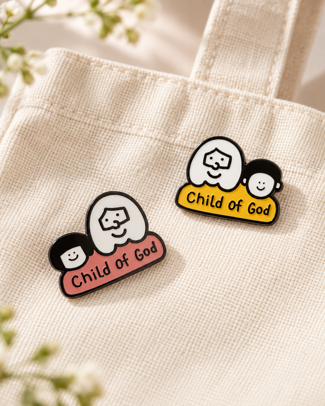 Pink and yellow Child of God Christian enamel pins displayed on a cream canvas tote bag in soft natural light