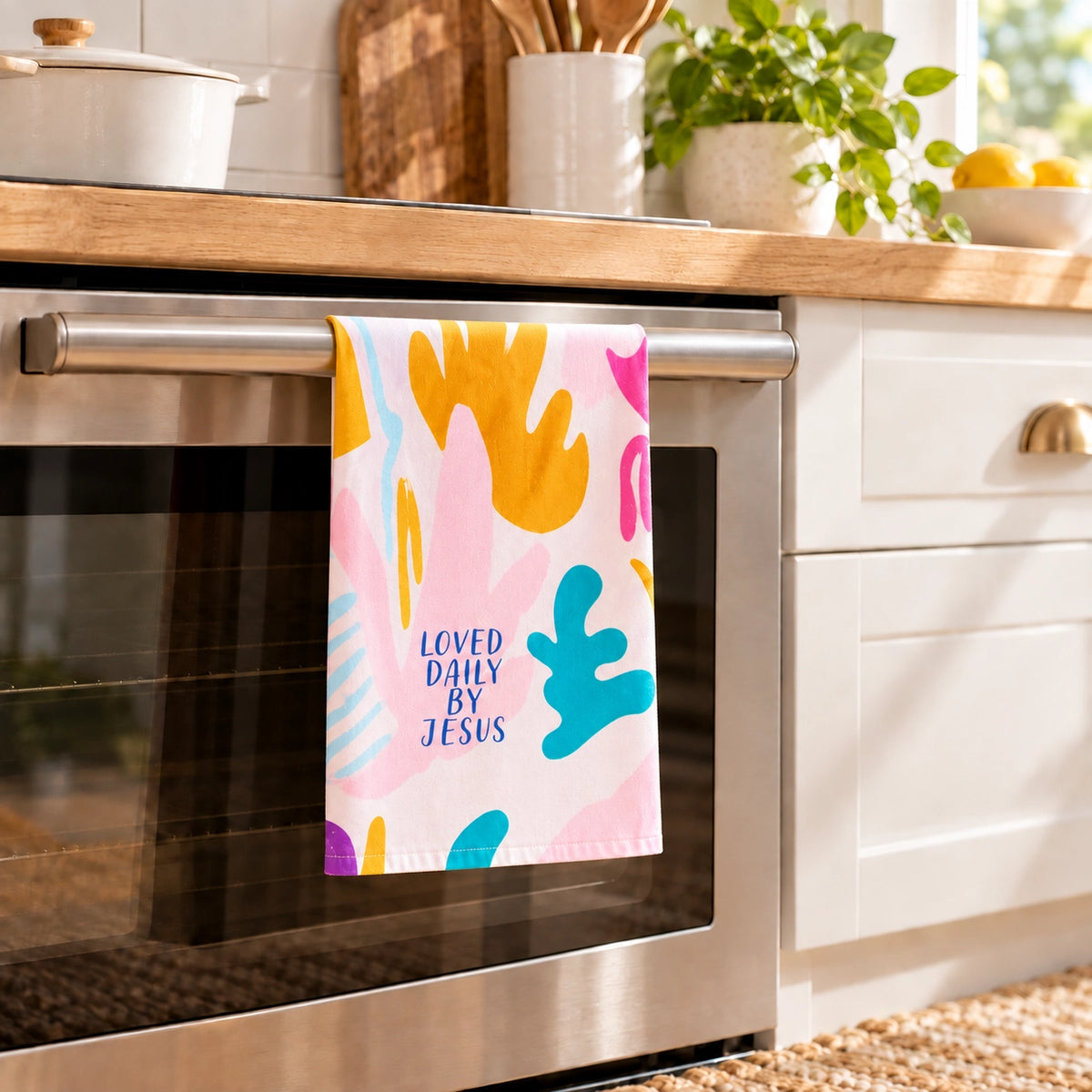 Loved Daily by Jesus colourful Christian tea towel hanging in one layer from an oven handle in a bright modern kitchen