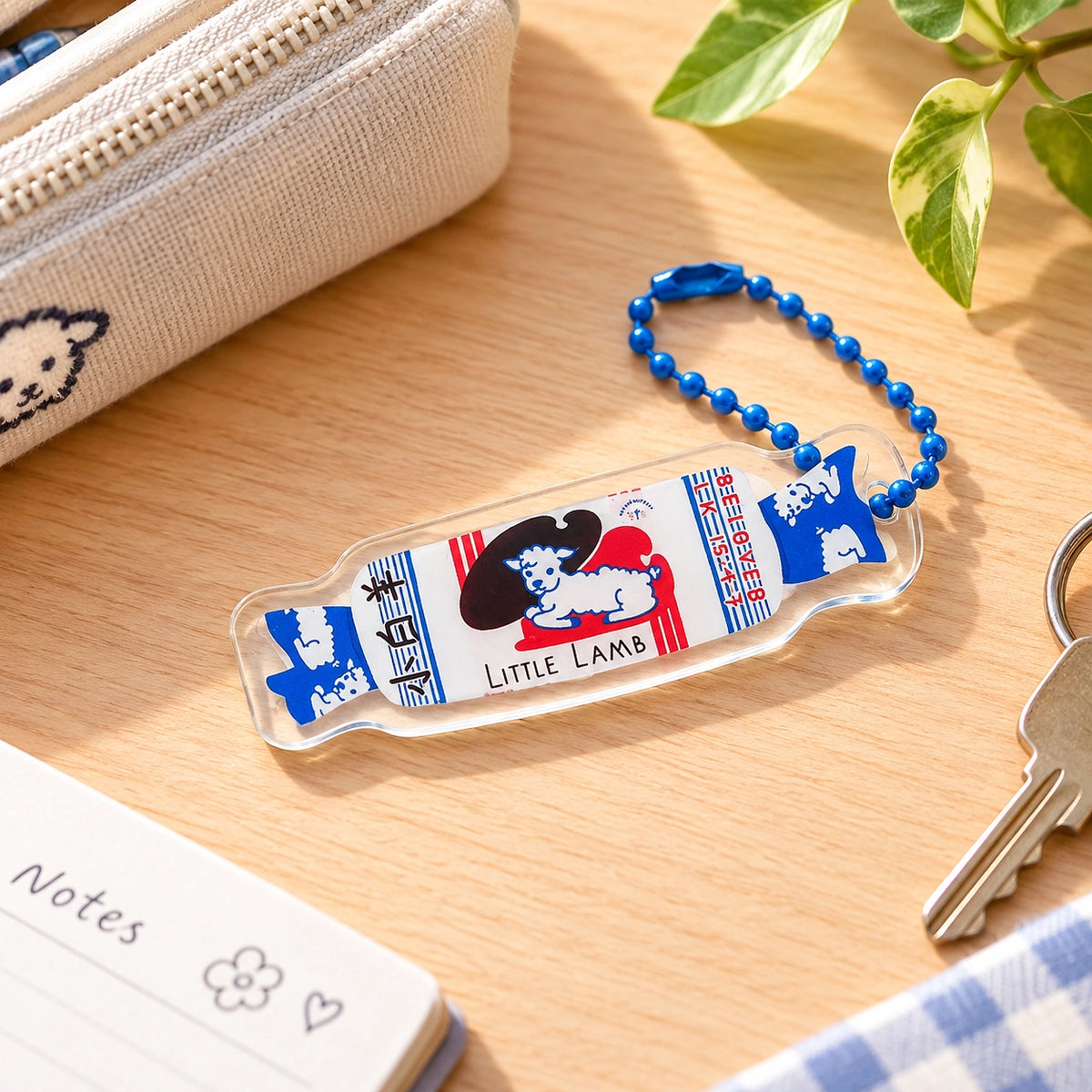 Beloved Little Lamb Sweet acrylic keychain styled on a warm wooden desk beside keys, a notebook and a cream pouch