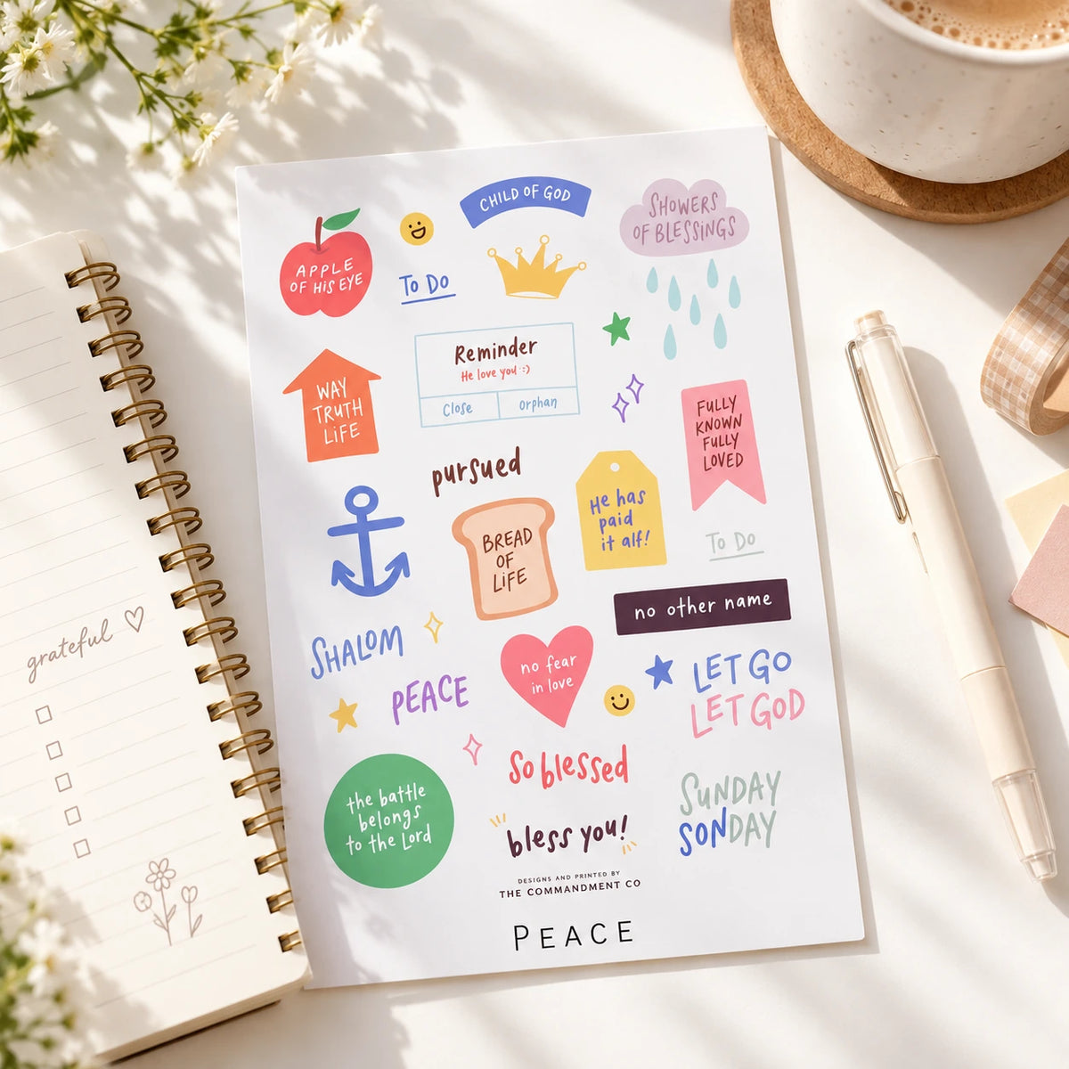 Peace journaling sticker sheet arranged beside a notebook and pen in a bright desk setting.
