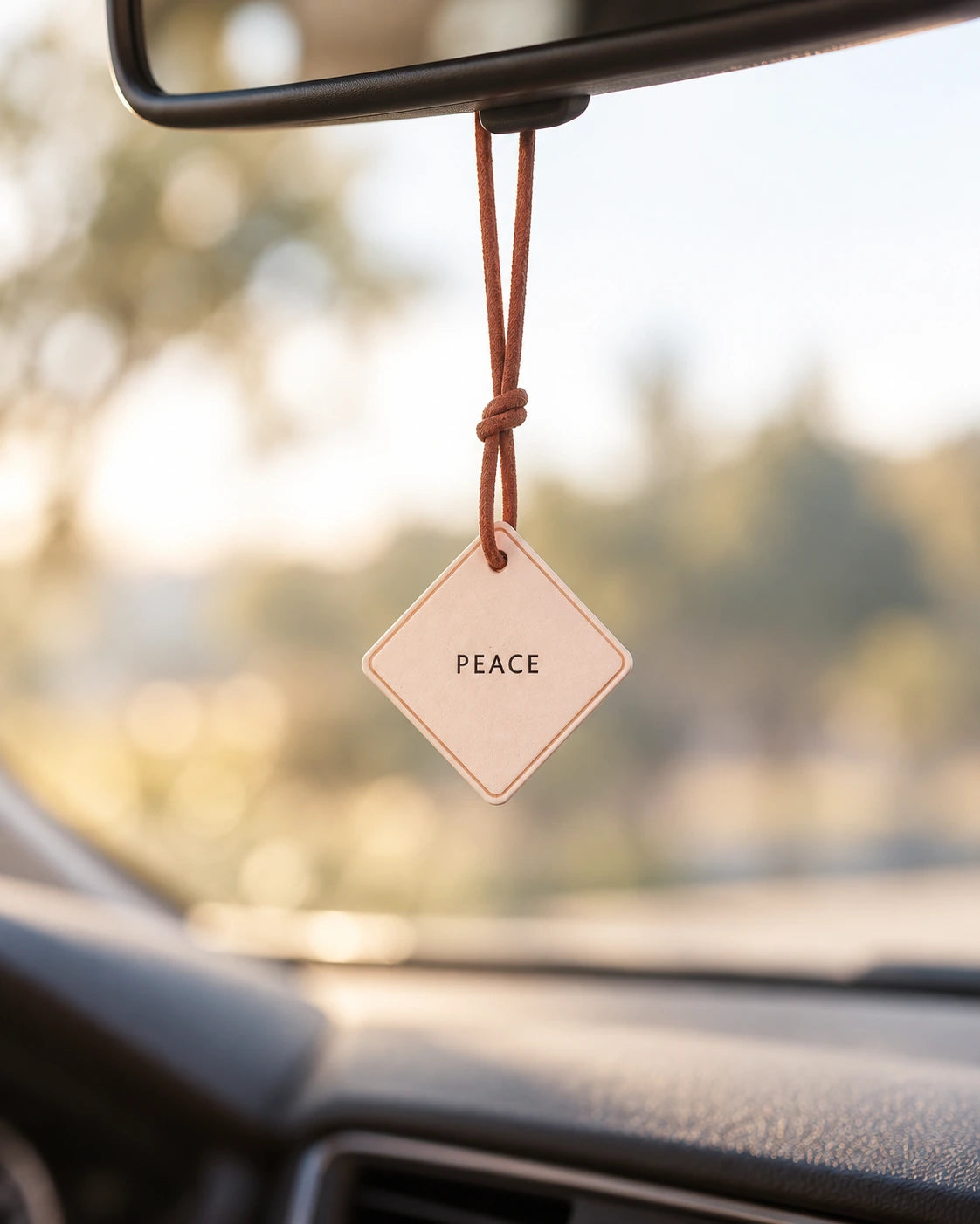 Peace leather car charm hanging from a rear-view mirror in warm natural light