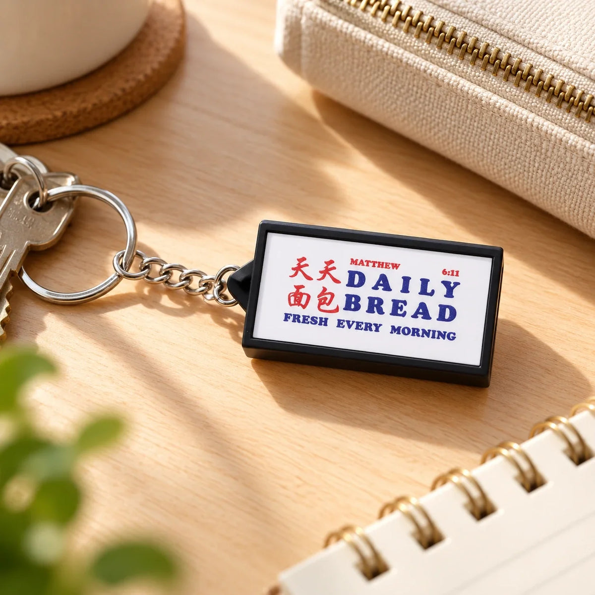 Daily Bread Matthew 6:11 lightbox keychain resting beside house keys and a notebook on a sunny wooden desk
