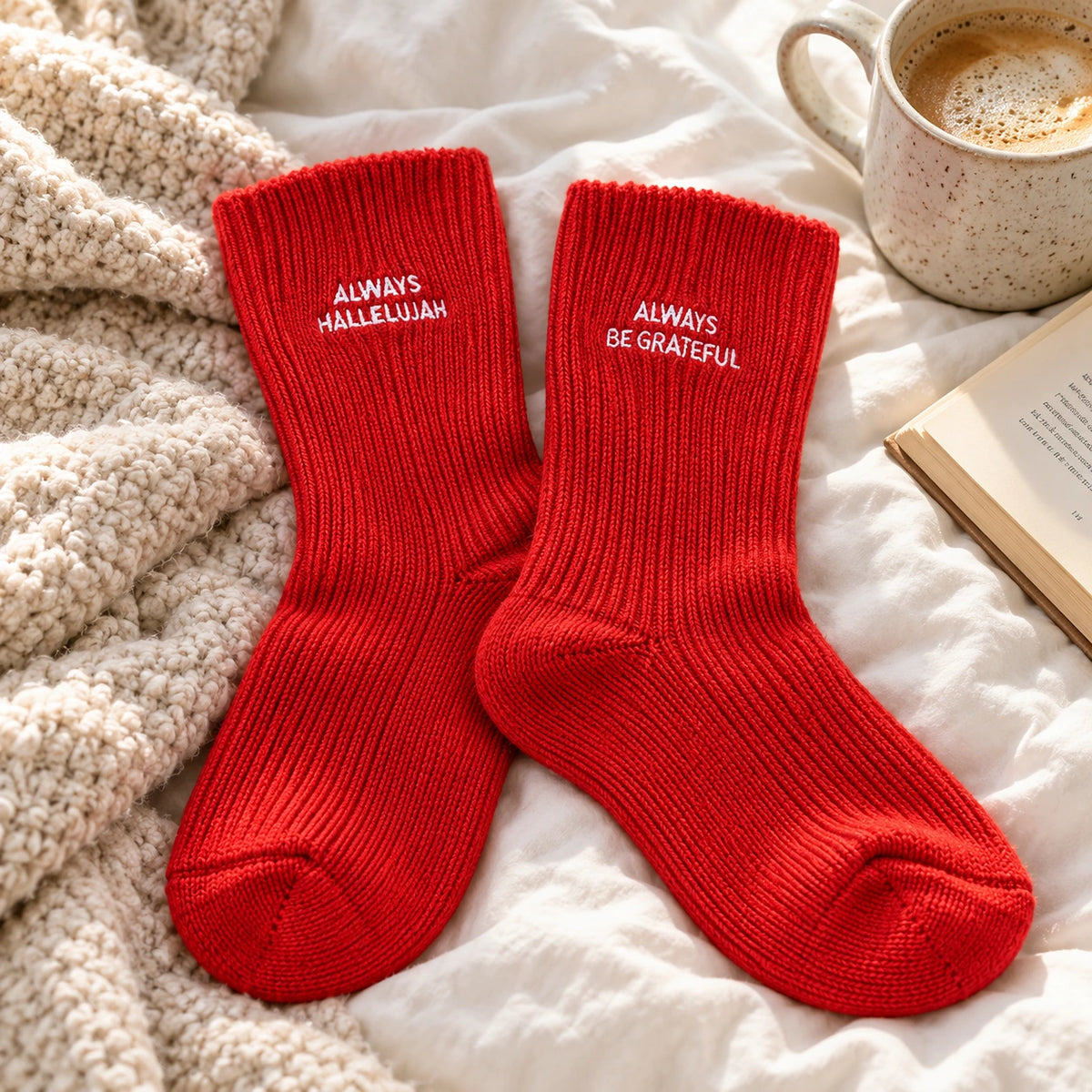 Red Always Hallelujah and Always Be Grateful Christian socks styled on soft bedding beside coffee and a book.