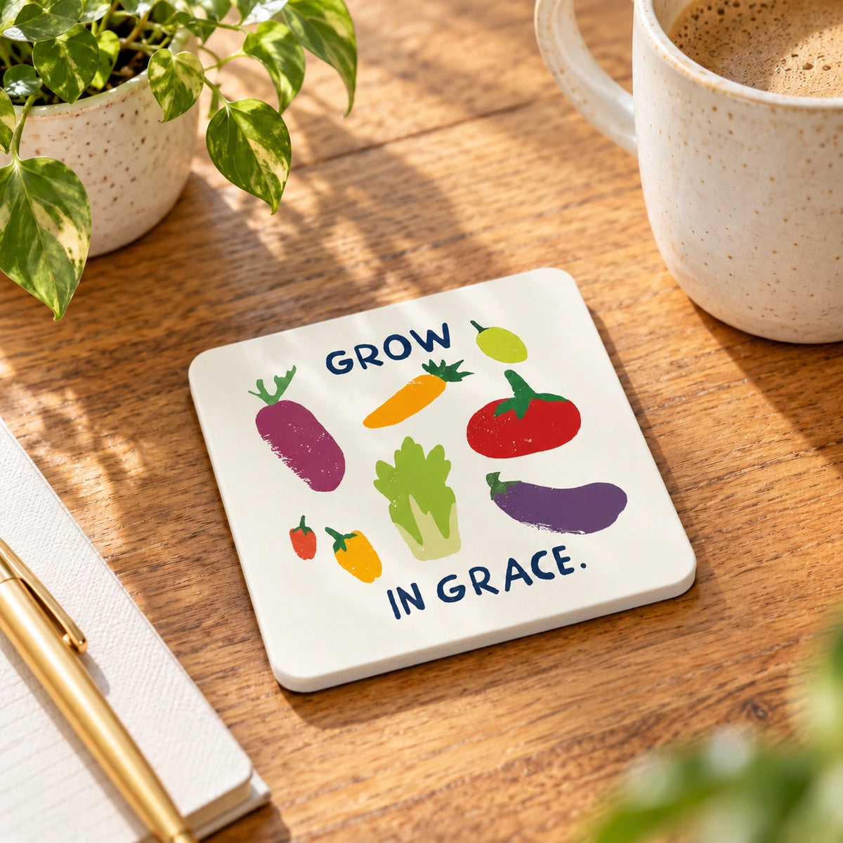 Grow in Grace illustrated vegetable coaster with white side edges on a wooden table beside a coffee mug.