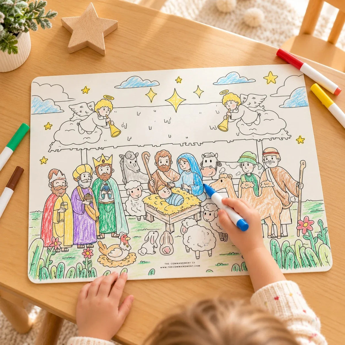 Child colouring the Nativity of Jesus mat with pens on a wooden table