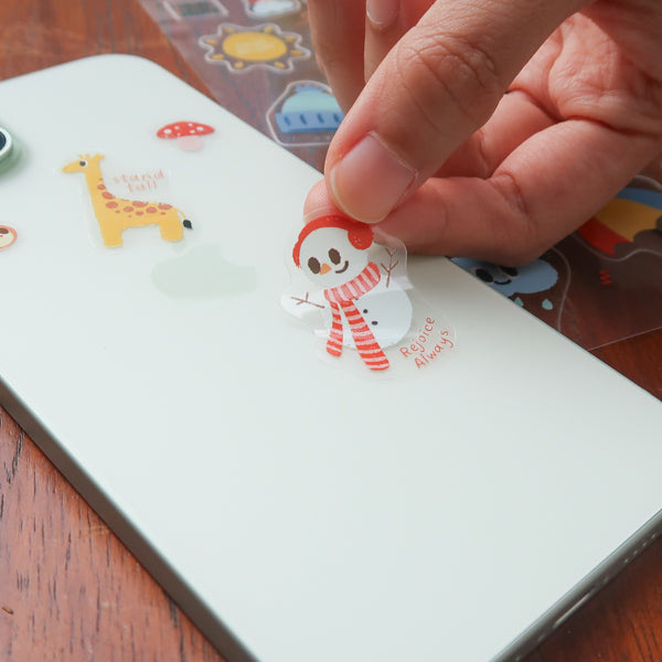 Hand placing a cute weather themed Christian sticker from the everyday believer sticker sheet onto a phone, featuring playful faith-inspired illustrations