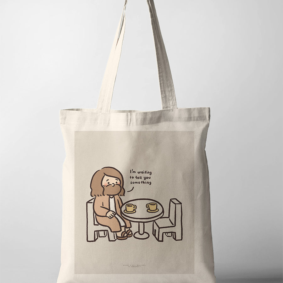 Canvas tote bag featuring a playful illustration of Jesus sitting at a table with coffee cups, saying 'I'm waiting to tell you something,' symbolizing patience and connection.