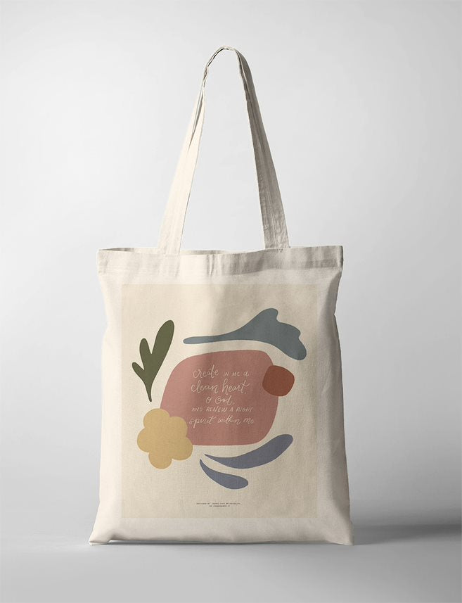 A minimalist Christian Tote Bag with abstract shapes in muted earthy tones. The center features the Bible verse 'Create in me a clean heart, O God, and renew a right spirit within me' in handwritten script.