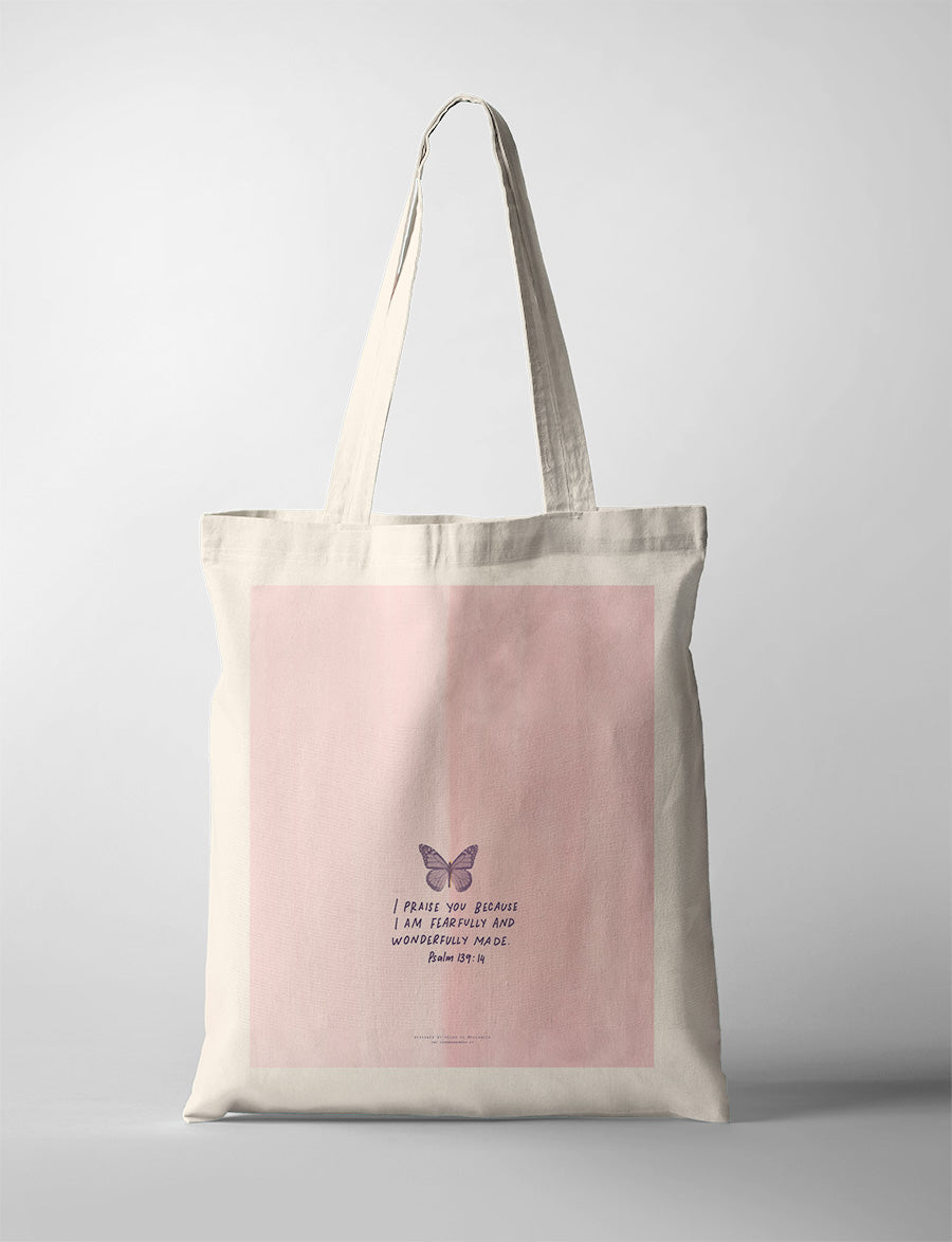 A soft pink tote bag with minimalist art featuring a delicate butterfly and the Bible verse Psalm 139:14: 'I praise you because I am fearfully and wonderfully made.' A simple yet elegant modern Christian gift for everyday use.