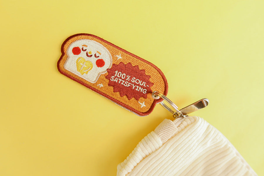 Fun embroidered keychain featuring a bread character and the inspirational message '100% Soul-Satisfying'.