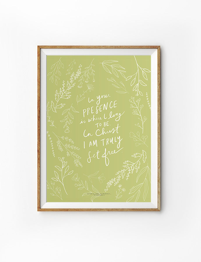 A Christian wall poster with a light green background and delicate white botanical illustrations surrounding a handwritten faith quote: 'In your presence is where I long to be. In Christ I am truly set free.' Framed in light wood, the design evokes peace, freedom, and spiritual intimacy