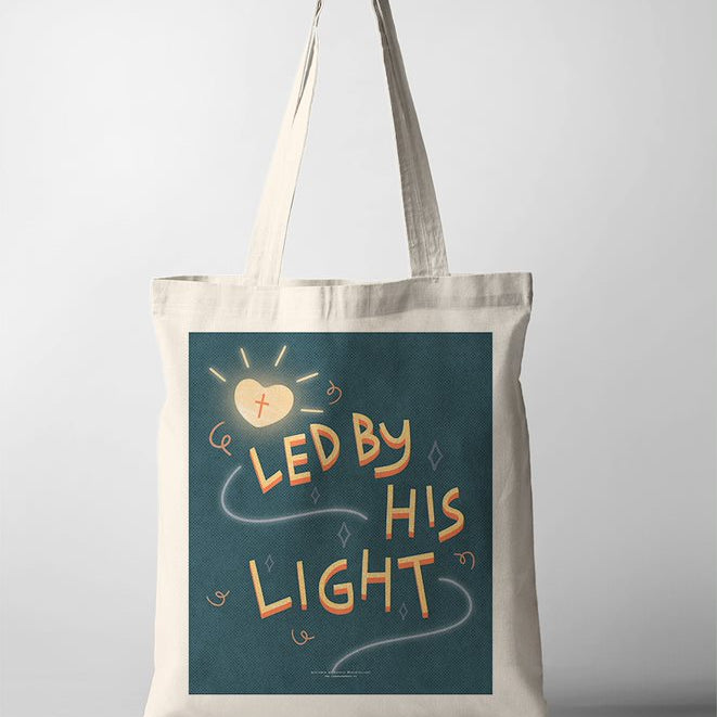 A faith based Tote Bag featuring an inspirational quote, "Led by His Light" displayed on a canvas tote bag. The design includes a glowing lantern amidst a dark teal background, emphasizing themes of hope and guidance. The uplifting message on the faith based poster encourages inner light and positivity