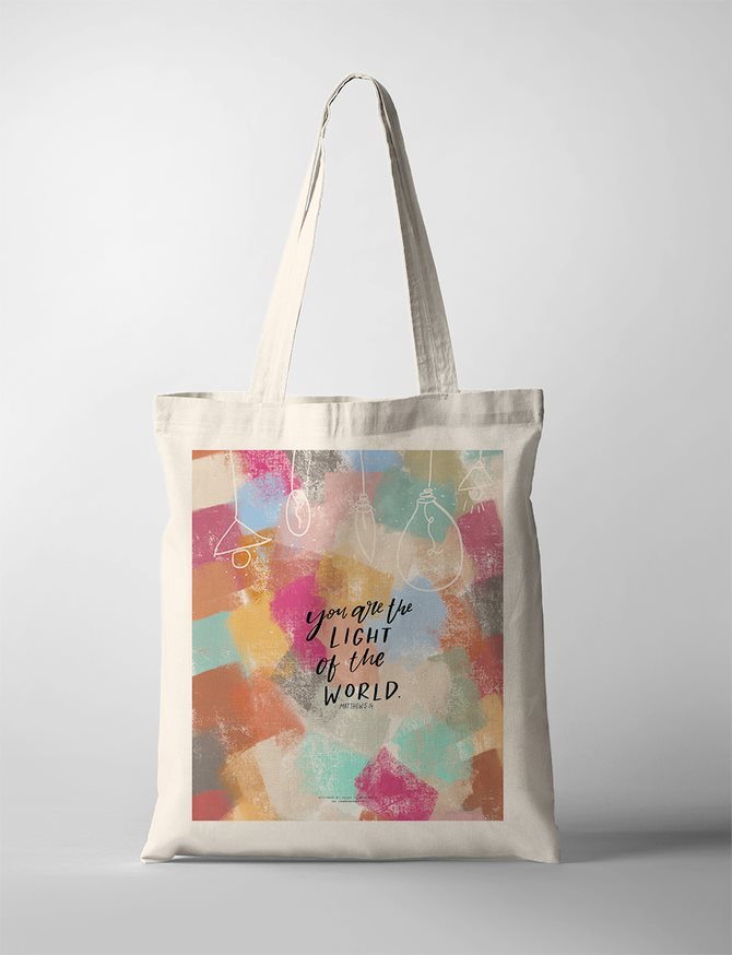Christian faith tote bag with colorful abstract background and hand-drawn light bulbs, featuring the Bible verse 'You are the light of the world' from Matthew 5:14. Inspirational Christian tote bag to carry and gifts.