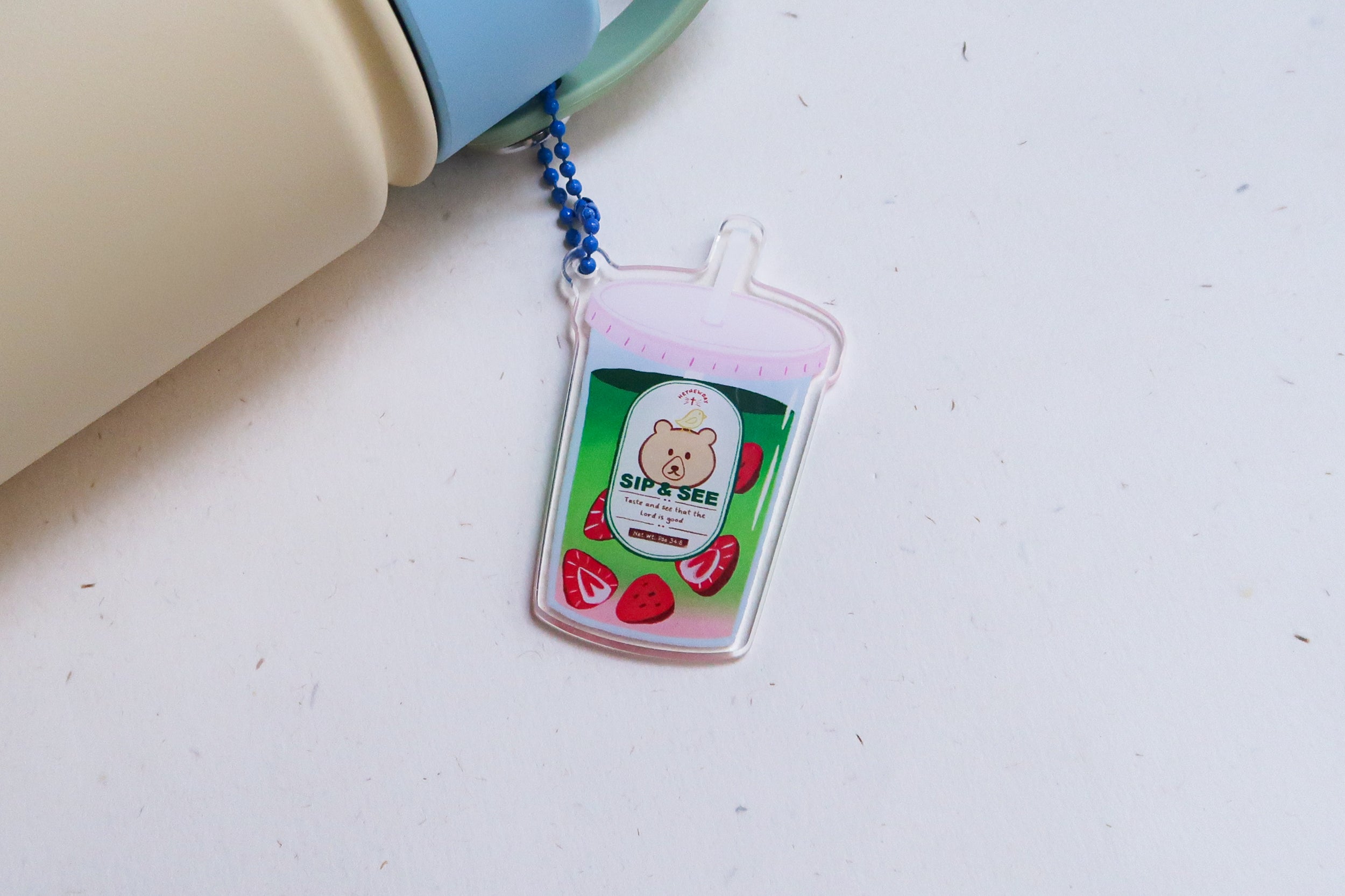 Sip & See strawberry matcha drink acrylic keychain attached to a water bottle, featuring a cute bear illustration and the verse “Taste and see that the Lord is good.”