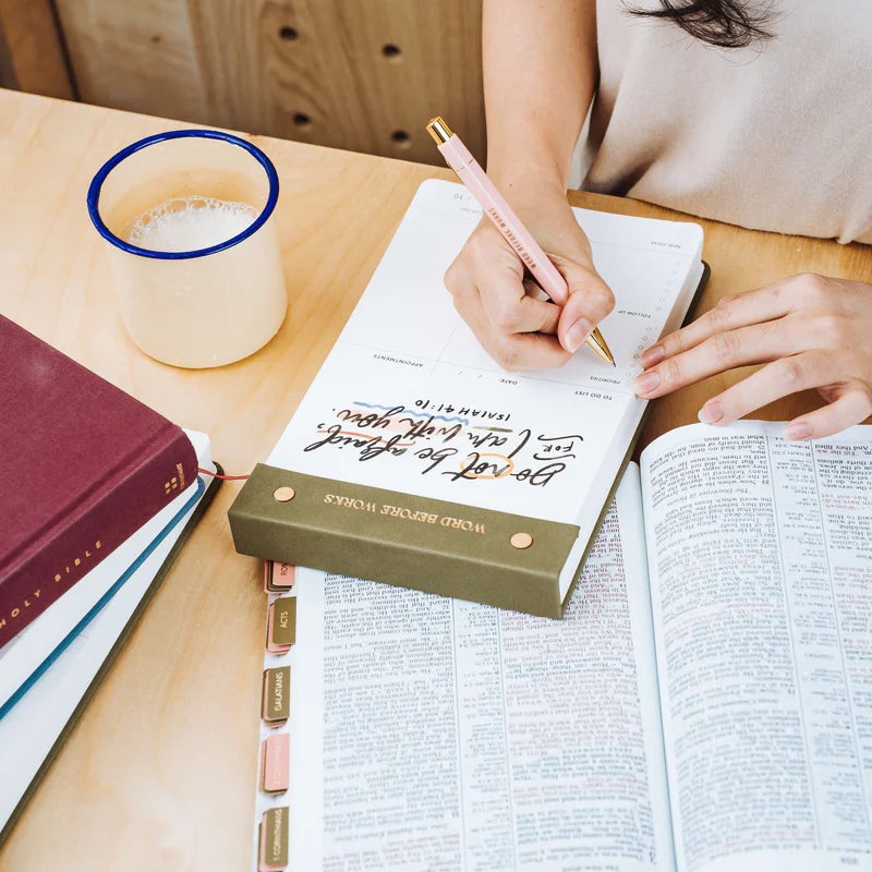 Woman writing on The Project J Christian notepad with "Do not be afraid, for I am with you" from Isaiah 41:10, alongside an open Bible and a cup of coffee, inspiring peaceful and faith-filled daily planning.
