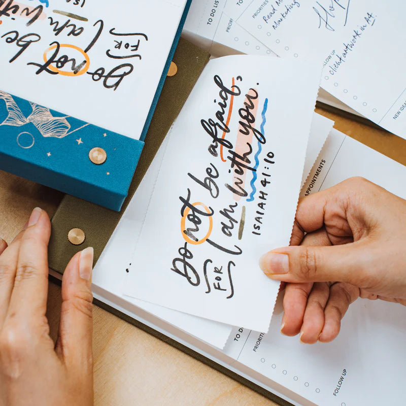 Hands tearing a page from The Project J Christian notepad featuring the inspiring verse "Do not be afraid, for I am with you" from Isaiah 41:10, perfect for uplifting daily planning and encouragement.