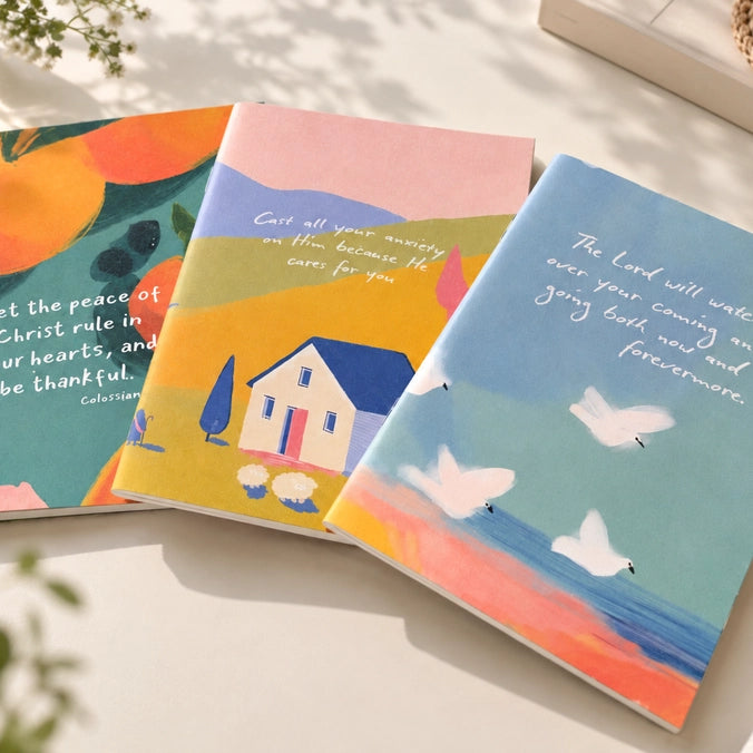 Three colourful A6 Christian notebooks with Bible verse covers arranged together in warm natural light