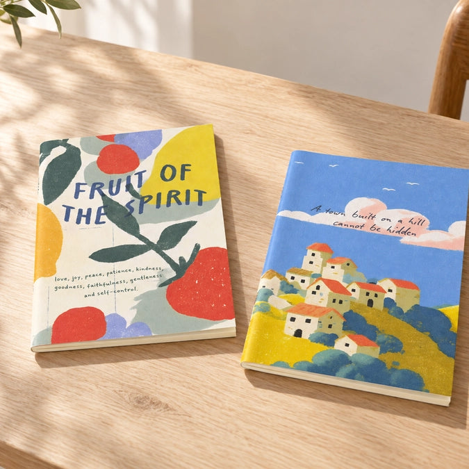 Fruit of the Spirit and A Town Built on a Hill A6 Christian notebooks displayed side by side on a wooden table
