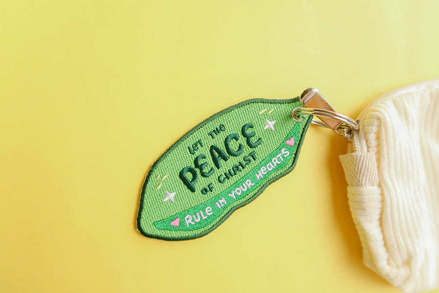 Green keychain with 'Let the Peace of Christ Rule in Your Hearts' embroidery.