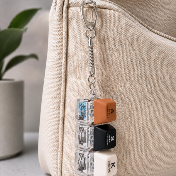 ASK SEEK KNOCK light-up keycap keychain clipped to a textured beige bag