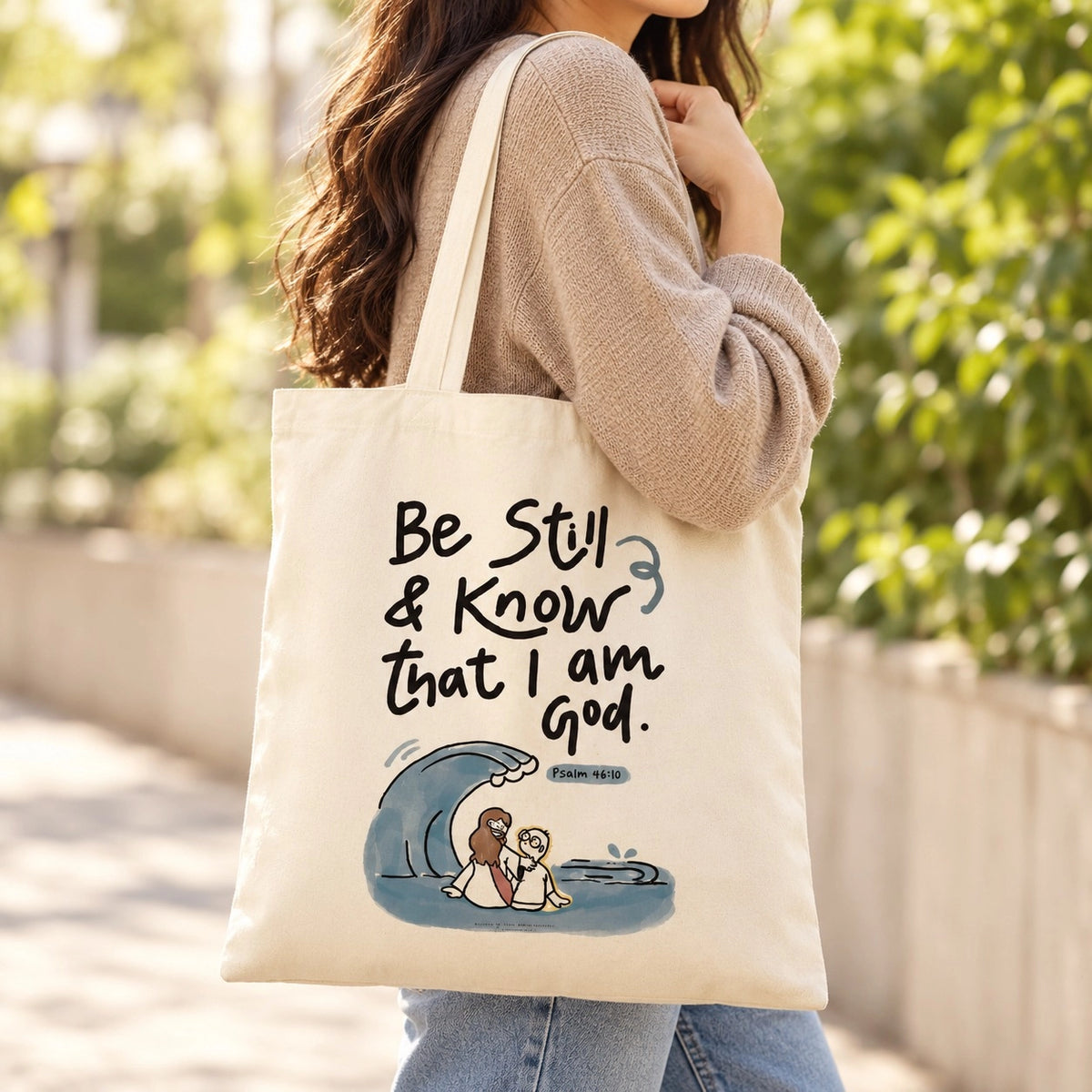 Be Still and Know That I Am God Psalm 46:10 cream canvas tote bag being carried over the shoulder outdoors.
