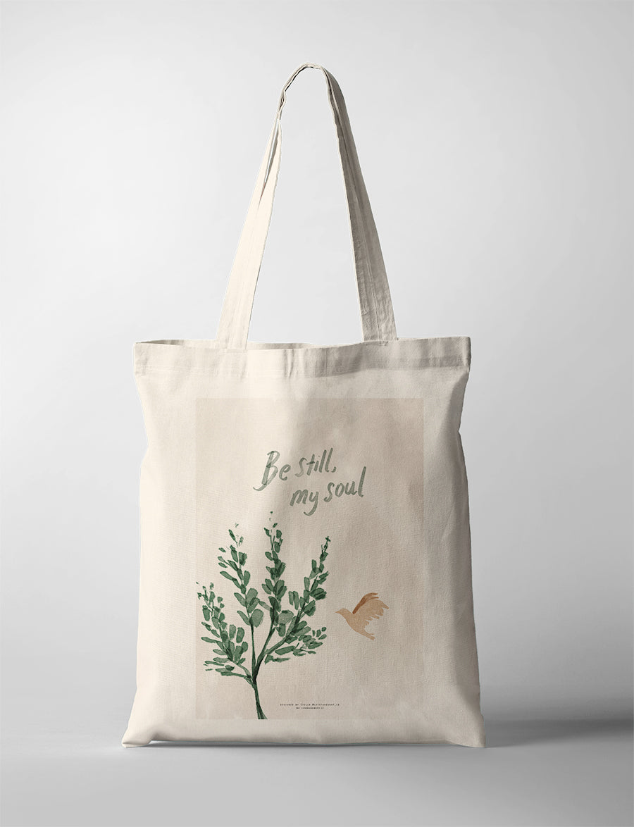 Christian tote bag featuring “Be Still, My Soul” with green botanical artwork and a flying bird illustration