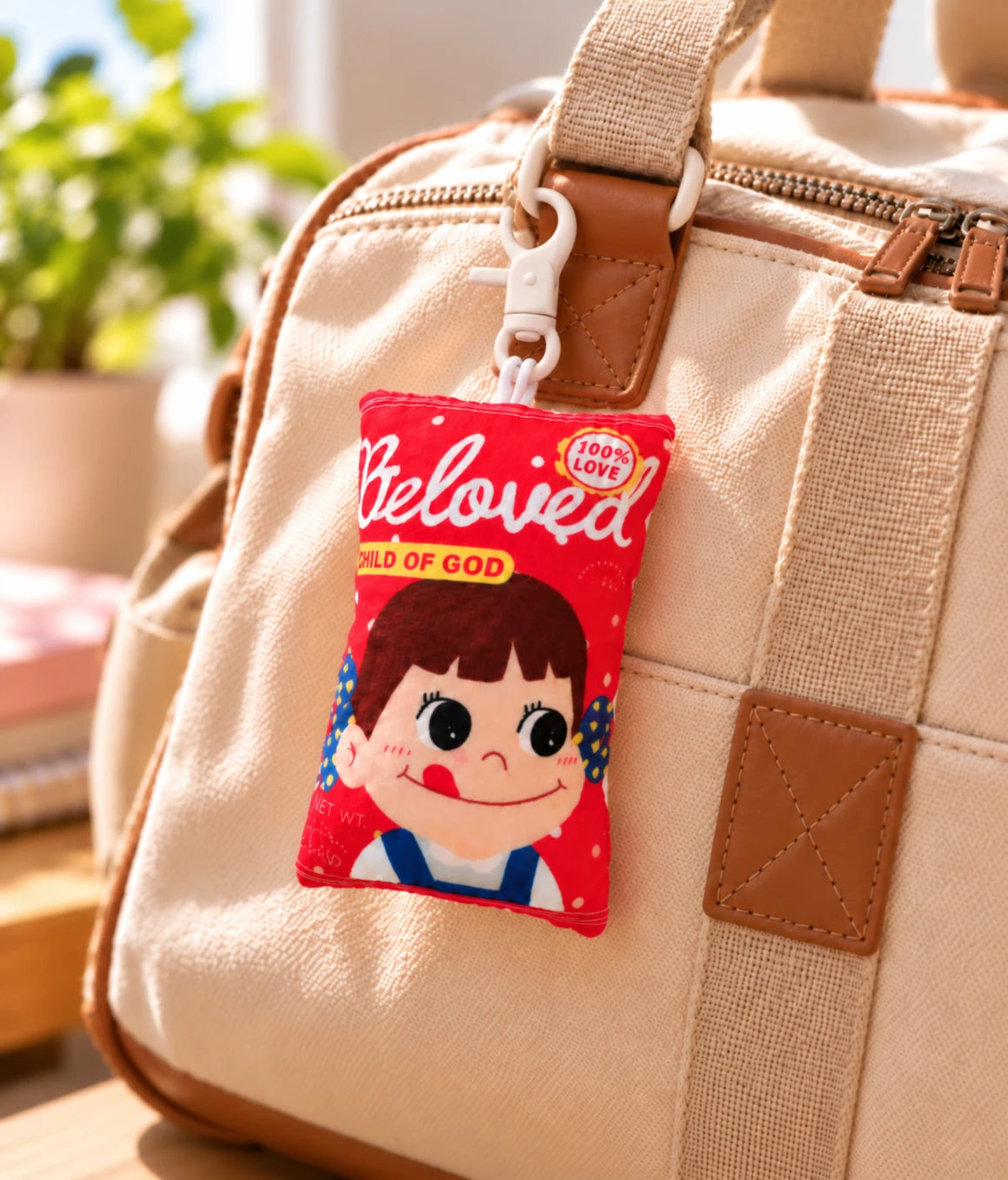 Beloved Milk Candy Girl red plushie keychain clipped to the strap of a beige canvas backpack in warm daylight