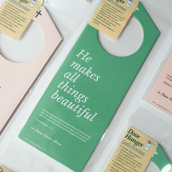Close-up of Christian door hanger packaging featuring inspirational Bible verses such as 'He makes all things beautiful,' 'His mercies are new every morning,' and 'I will give you rest,' with a focus on God's promises.