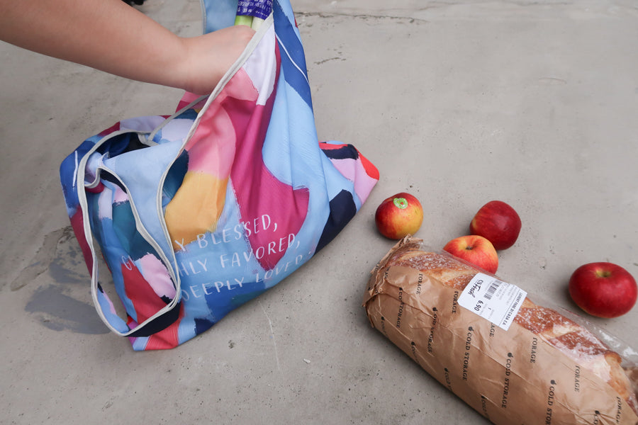 Hand reaching into a
colorful foldable reusable
Bible verse shopping bag
with groceries, perfect for
Christian gifts from a
Christian gift store.
