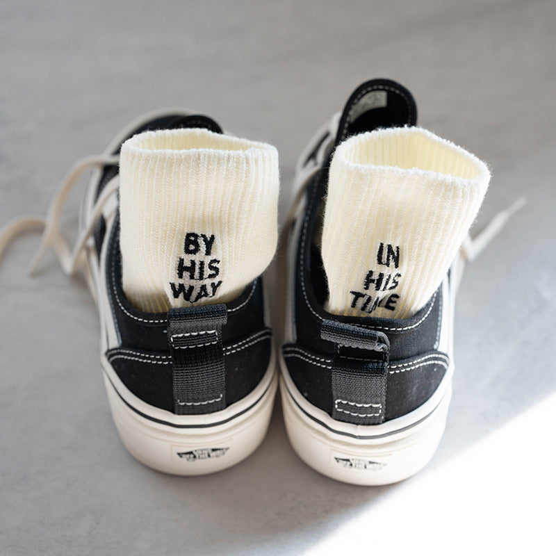 Cream ribbed-knit socks embroidered with "BY HIS WAY" and "IN HIS TIME" shown inside black sneakers — a faith-inspired accessory from The Commandment Co.