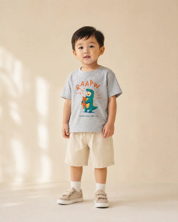 Young child wearing the grey RAAAW dinosaur kids T-shirt with beige shorts
