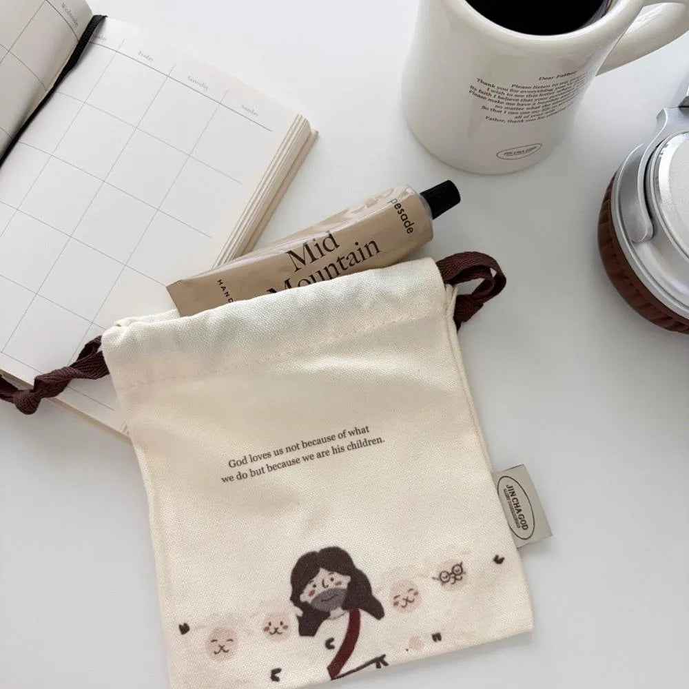 God Loves Us canvas drawstring pouch with a Jesus and sheep illustration, styled with a planner, coffee and everyday essentials