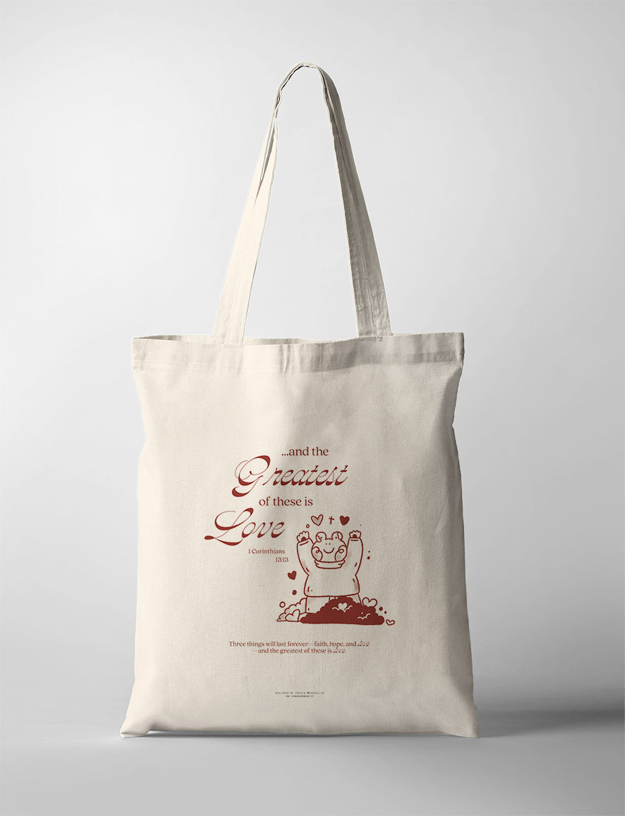 Natural canvas Christian tote bag featuring a joyful bear illustration and The Greatest of These Is Love from 1 Corinthians 13:13.