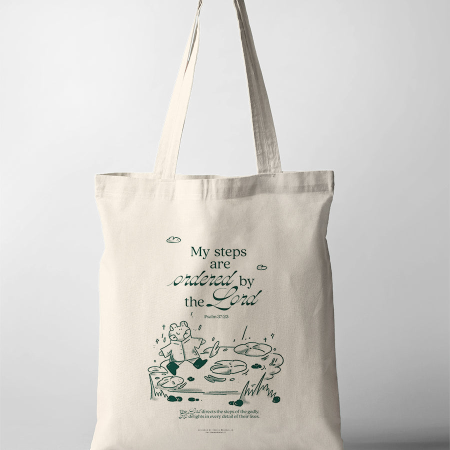Natural canvas Christian tote bag with a bear walking across stepping stones and the words My Steps Are Ordered by the Lord.