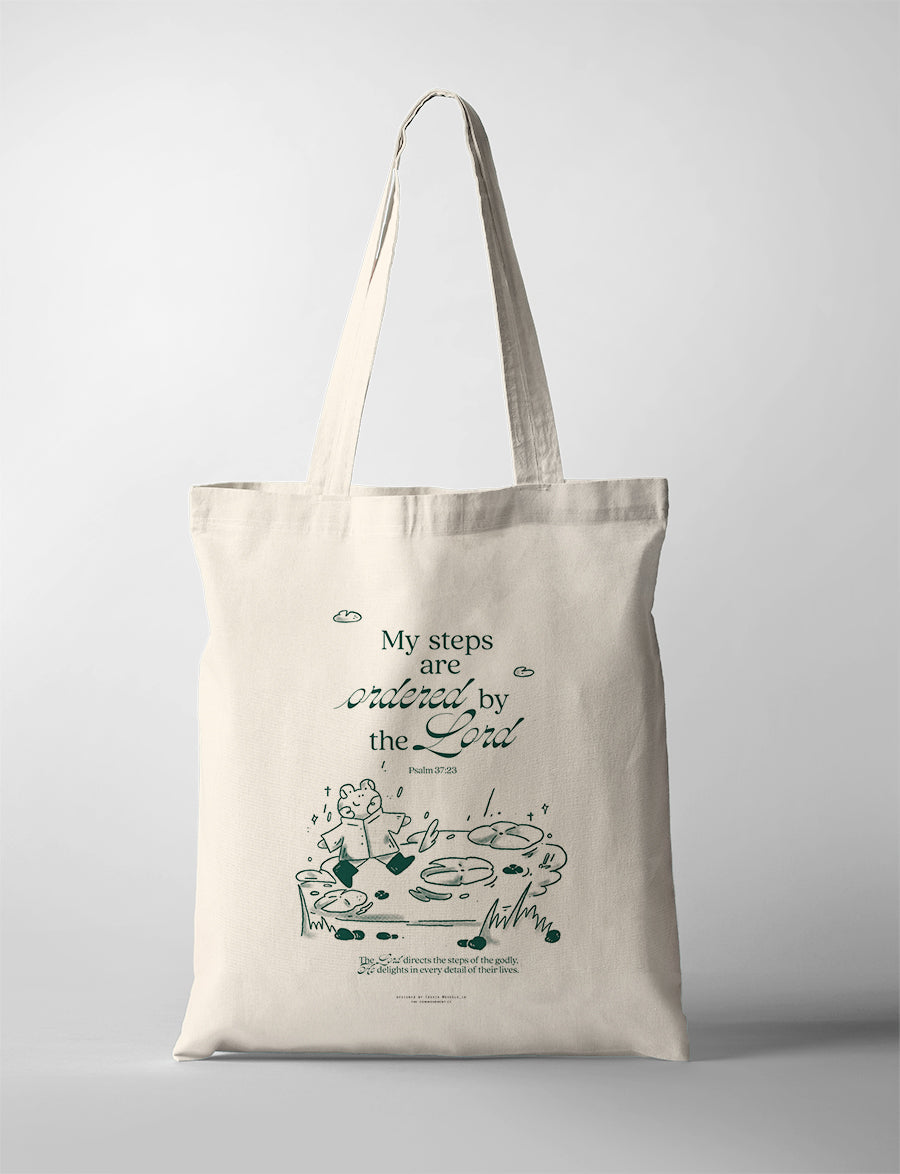 Natural canvas Christian tote bag with a bear walking across stepping stones and the words My Steps Are Ordered by the Lord.