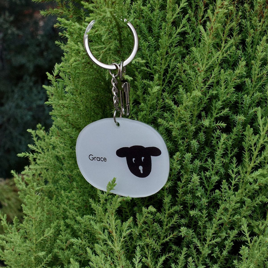 Christian keychain with "Grace" and a sheep design hanging on lush green foliage, symbolizing faith and serenity.