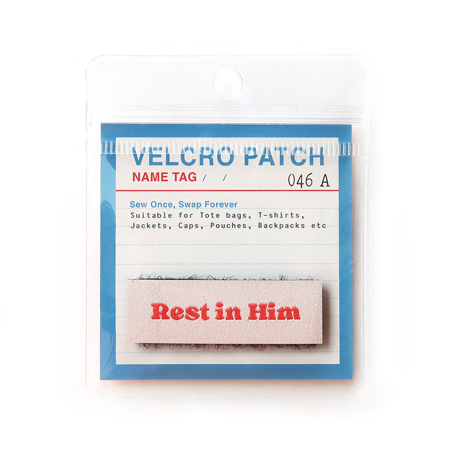 Light pink Velcro tag with red text 'Rest in Him,' a faith-based embroidered patch for Christian apparel and accessories.