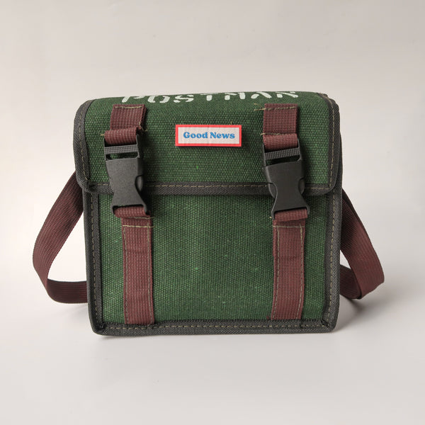 A green canvas messenger bag with 'Good News' branding on the front, featuring brown straps and a durable design. The bag is faith-themed with a minimalist, rugged look suitable for daily use.