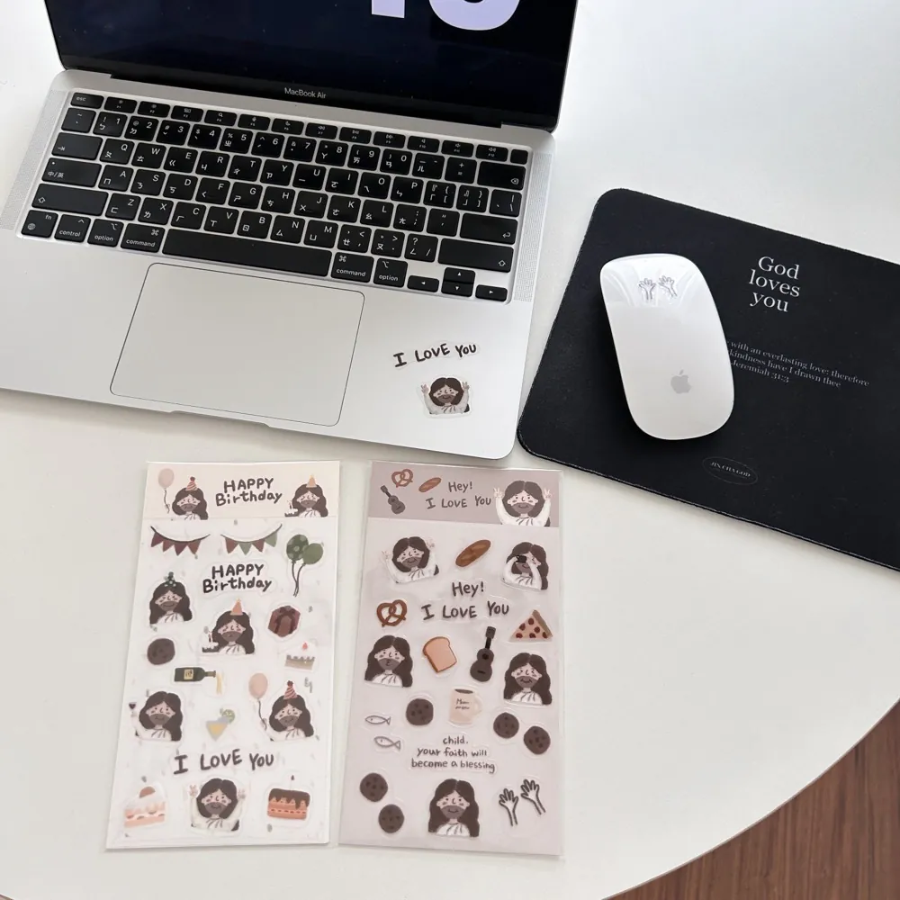 Laptop with "I Love You" Jesus sticker, two Christian sticker sheets, and a "God loves you" mouse pad and mouse on a white desk, inspiring encouragement and simple happiness.