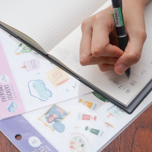 Hand placing a cute Christian sticker from everyday believer sticker sheet onto a planner, showing journaling and faith-inspired sticker use