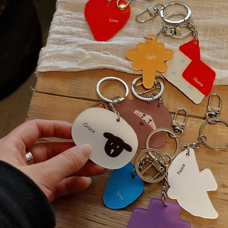 A collection of colorful Christian-themed keychains with words like "Grace," "Love," and "Peace," displayed on a wooden surface, reflecting faith and inspiration.