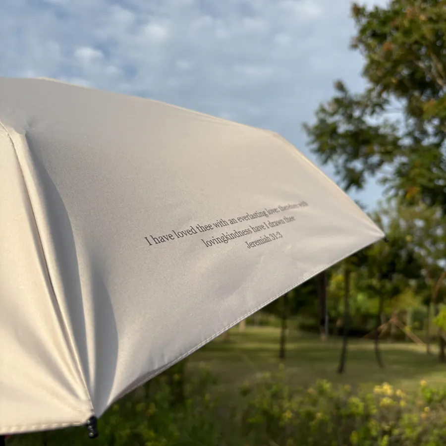 Christian umbrella with “Enjoy today in the love of God” message, held by someone in a grassy park, inspirational faith accessory from The Commandment Co Singapore.
