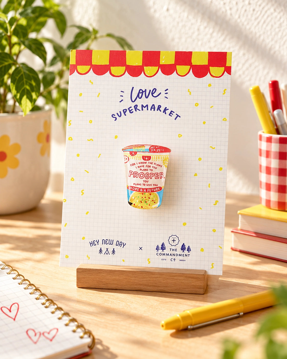 Cup Noodles Prosper LOVE SUPERMARKET acrylic pin displayed on a sunny desk in its illustrated backing card.