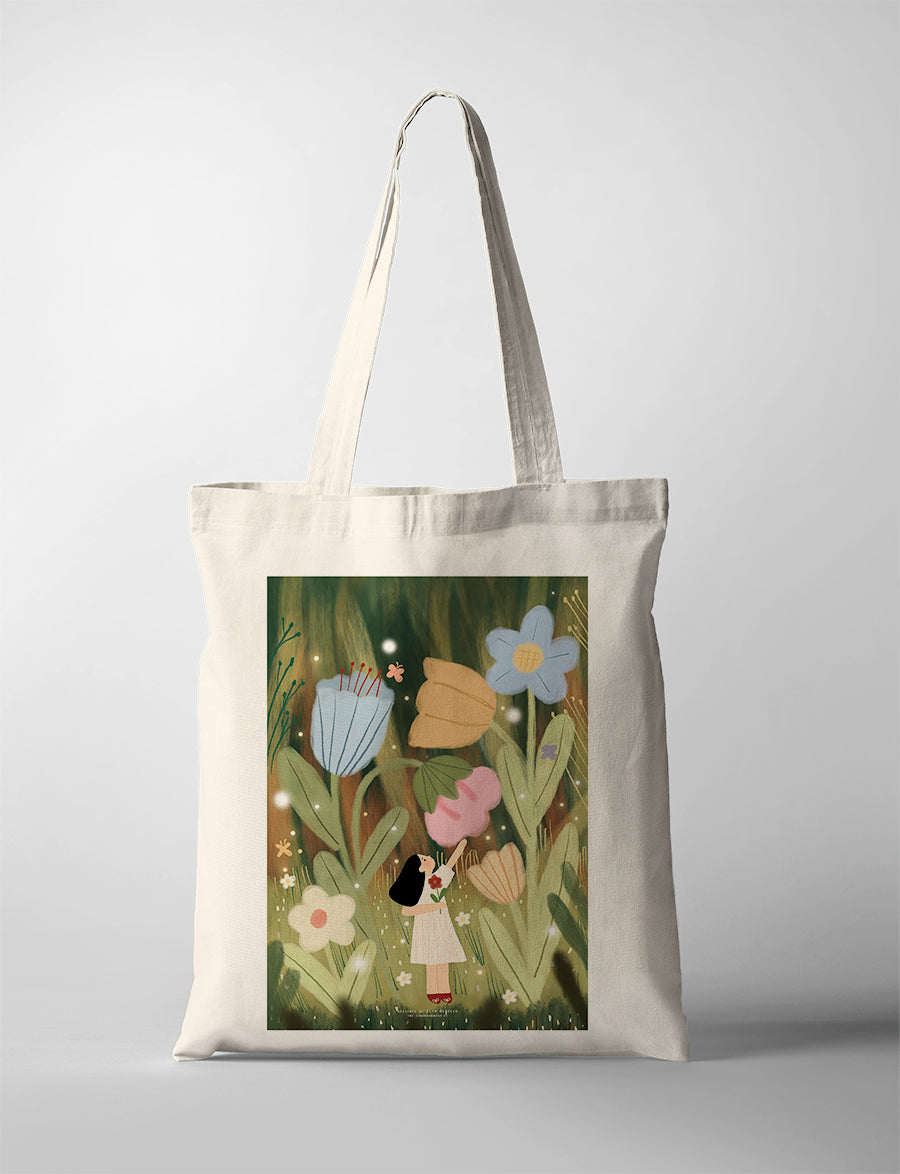 Canvas tote bag featuring Dita artwork of a girl standing among large whimsical flowers in a green field, soft storybook style illustration