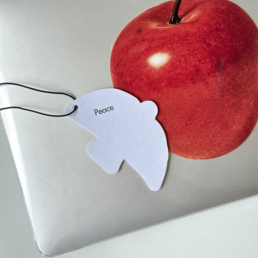 White dove-shaped heart scent tag with the word "Peace," symbolizing encouragement and simple happiness, placed on a laptop with a red apple sticker.