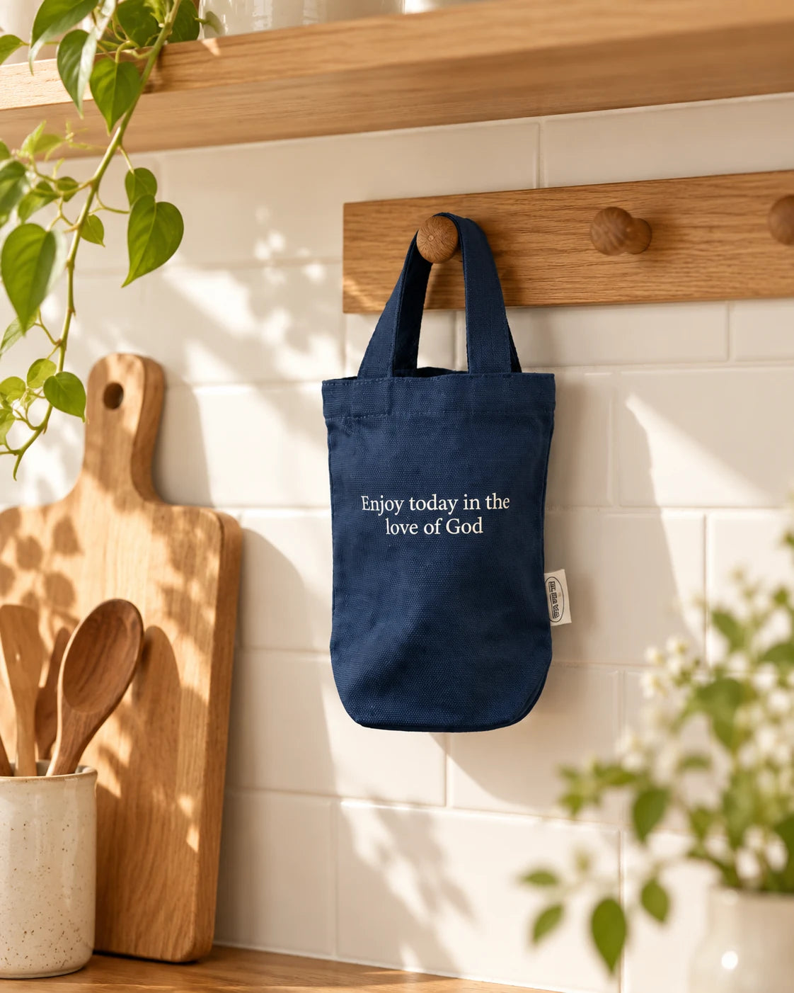 Enjoy Today in the Love of God navy beverage bag hanging from a wooden hook in a bright homely kitchen