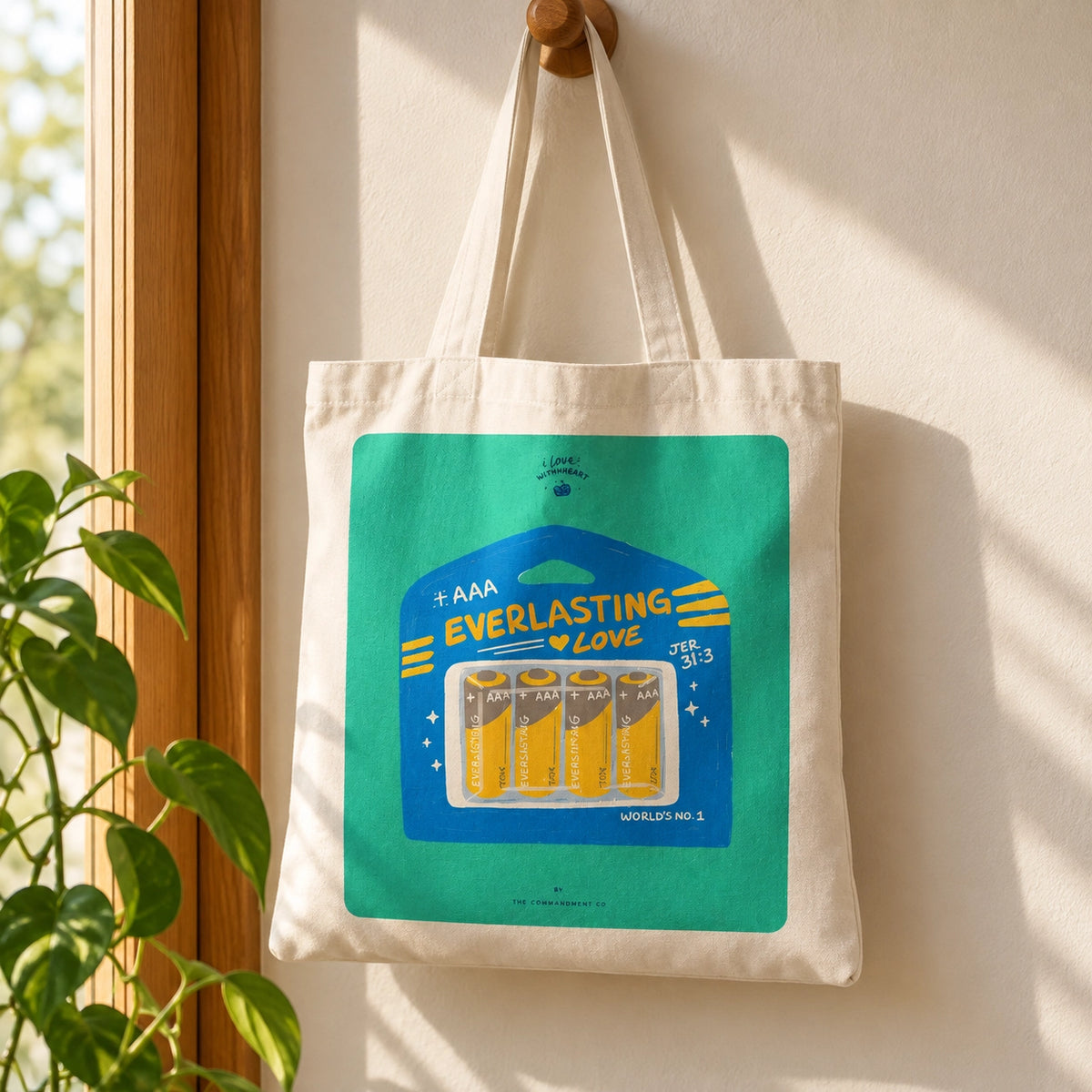 Everlasting Love Battery AAA tote bag hanging on a wooden wall hook in warm natural light.