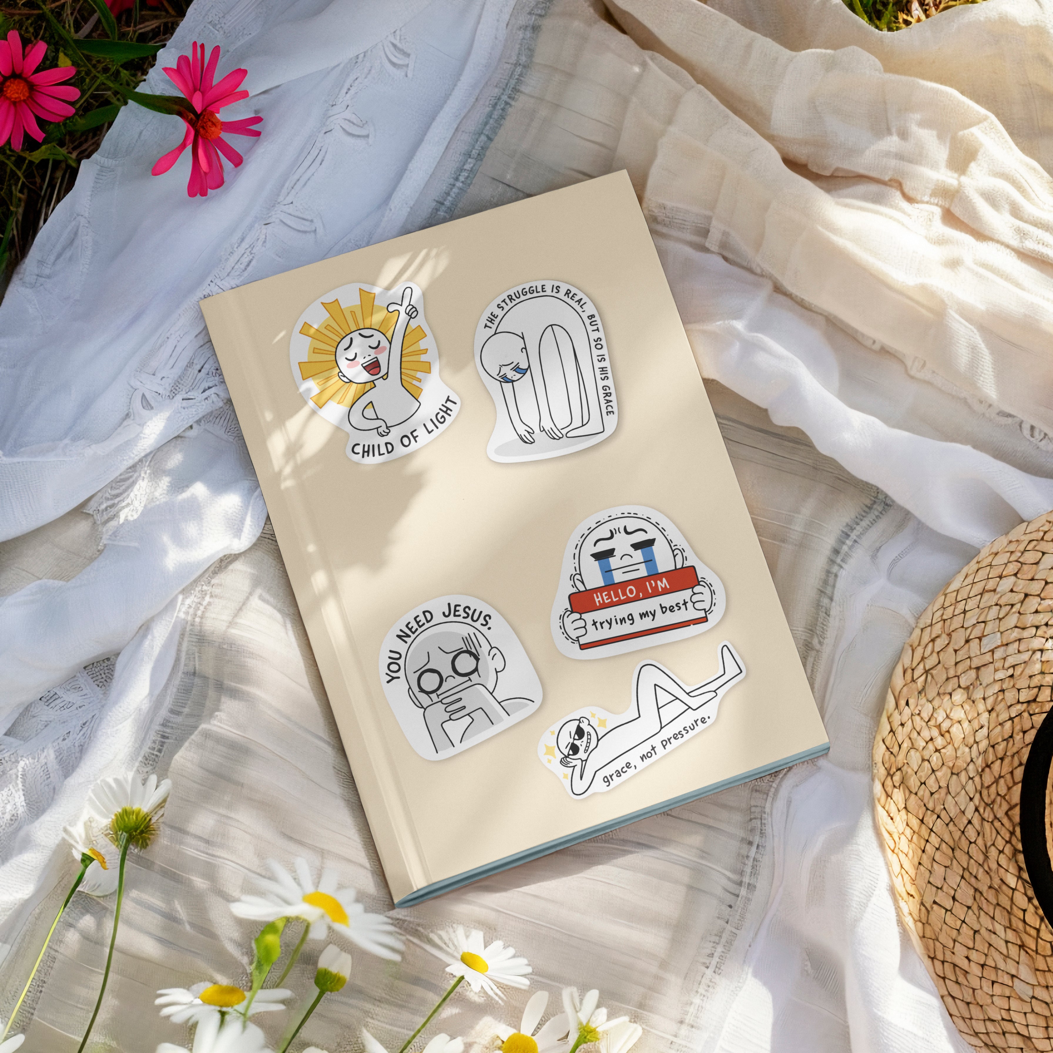 Journal decorated with Everyday Believer stickers featuring Christian messages like "Child of Light" and "Grace, Not Pressure," surrounded by flowers, from The Commandment Co, Singapore.